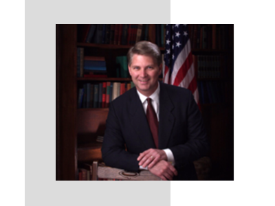 A man in suit and tie sitting next to an american flag.